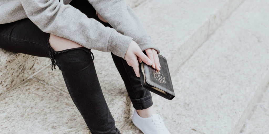 person-sitting-holding-bible-ripped-jeans